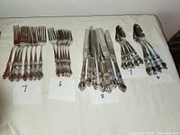 Full view of all flatware pieces arranged in groups on a white surface with quantity labels showing 7 dinner forks, 6 salad forks, 8 knives, and 7 spoons.