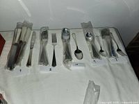 Photo showing various wrapped flatware pieces including knives, forks, spoons, and extras labeled with numbers 7, 8, 9, 10 showing seating for seven plus extra pieces.