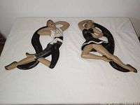 Pair of vintage chalkware/plaster wall decorations on white cloth showing male and female figures reclining in theatrical poses with black backdrops.