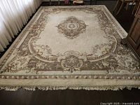Full view of large wool carpet laid on dark hardwood floor, showing full design and fringe.