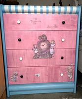 Front view showing pink painted drawers with black and white knobs, and Alice in Wonderland character scenes including Cheshire Cat and Alice.