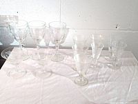 Photo showing full set of 10 etched glassware pieces on white tablecloth: 2 wide coupe glasses, 4 goblet style glasses, 4 smaller sherry/wine glasses with floral etched pattern.