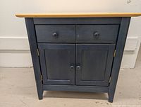 Front view of blue wooden cabinet showing shape, drawer, double doors, knobs, and natural wood top.