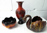 Three ceramic pottery pieces: swan planter, flower-shaped planter, and tall vase, shown from the front on white surface