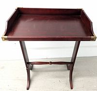 Front view of the fully assembled butler's tray table, showing the wooden tray with raised edges and brass corner details resting on the foldable stand.