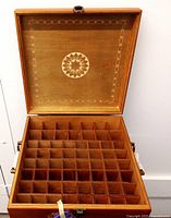 Open wooden box showing 64 individual square compartments with dividers inside, interior bottom and lid with decorative geometric pattern.