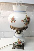 Full view of lamp showing white milk glass globes with floral decoration and brass holder with ornate metal base.