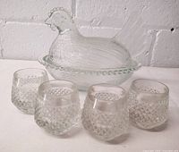 Photo showing vintage clear glass hen on nest dish with lid and 4 small clear textured glasses in front.