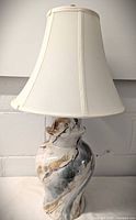 Full image of the lamp showing the off-white bell-shaped fabric shade and the marbled ceramic base with brown, gray, black, and white swirls in a ginger jar shape.