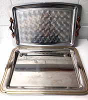 Two metal trays positioned upright, one with brown metal handles and textured interior, the other plain with gold trim and some wear visible
