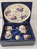 Miniature tea set pieces arranged in presentation box with floral decoration on porcelain and gold accents.