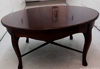 Front angle view showing the round wooden coffee table with cabriole legs on a light floor.