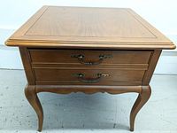 Front view of wooden side table showing two drawer fronts and curved legs