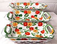 Three hand-painted ceramic baking dishes nested inside a white wire rattan carrier.