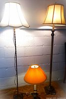 Three lamps visible: two floor lamps with traditional shades, one small table lamp with an orange pleated shade on a brass candlestick base.
