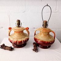 Photo showing two vintage Medalta pottery lamps side by side, both reddish brown with mottled glaze and new wiring, with one socket missing a harp and the other with harp.