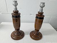 Pair of wooden oak candlesticks with metal tops against a white wall background.