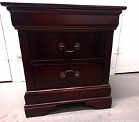 Front view of dark brown wooden nightstand with two drawers and metal handles, showing overall condition and style.