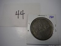 Front of 1960 Canadian silver dollar showing voyageur and indigenous person in a canoe with date and 'Canada Dollar'. Coin mounted in white cardboard holder.