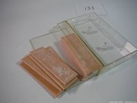 Eleven peach-colored rectangular wax packs with white powder residue, some stacked inside a clear plastic holder with two pegs to show quantity and condition.