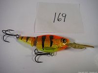 Side view of the orange and yellow Jointed Shad Rap with black stripes, showing front half with the diving lip and front treble hook.