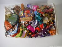Large clear plastic bag filled with assorted colorful vintage toys including figures, vehicles, and play accessories.