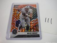 Front side of the Maxx Crosby 2021 Mosaic Orange Prizm football card showing the player in Raiders uniform with orange mosaic background and holographic effect.