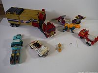 Main overview showing Optimus Prime truck and trailer, white sports car Transformer, light blue robot Transformer, small yellow figure, two purple dinosaur Transformers, and red cement mixer Transformer.