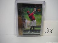 Front view of the 2001 Upper Deck Tiger Tales #7 Tiger Woods golf rookie card showing Tiger Woods in mid swing wearing red shirt and cap.