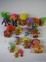 Overhead view of 16 vintage Treasure Troll collectible figures with various colorful hair and some with accessories, arranged on a white background.