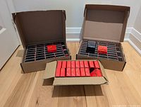 Three cardboard boxes filled with numerous black coin boxes, several red TD branded outer packaging boxes visible.