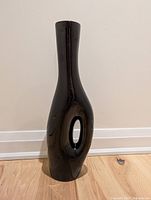 Front view of the glossy black pottery vase showing the tall, slender shape with central oval cutout.