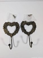 Two metal heart wall hooks with floral design laid flat including plastic bags with mounting screws.