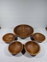 Top down view of 1 large wooden bowl surrounded by 4 smaller wooden bowls showing the shape, size, and wood grain finish of the bowls.