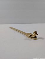 Close-up of vintage brass duck letter opener angled showing duck head detail and tapered blade.