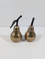 Front and side view of two brass pear-shaped salt and pepper shakers with dark metal stems and dispensing holes, showing condition and design details.