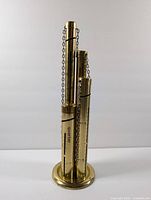 Front and side views reveal the four vertical tubes labeled for different US coins with caps chained to tubes, showing engraved markings and overall metal gold-tone finish.