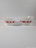 Two white milk glass bowls with red floral decoration and Frigidaire logo, front view side by side on white surface