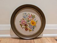 Front view of the circular embroidery art framed in plastic with wood-like finish.