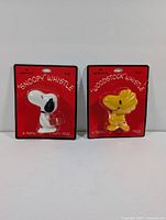 Both whistles in original packaging side-by-side against a neutral background showing front of packages with red card and plastic blister.