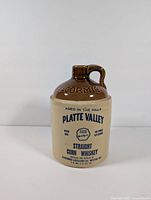Front view of ceramic whiskey jug showing blue printed text 'Platte Valley Straight Corn Whiskey' and brown glazed top
