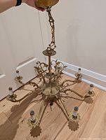 Full view of chandelier showing 8 arms with intricate gold tone metal ornate scrolling and leaf design, hanging chain on top.