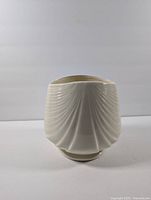 Front view of cream colored ceramic vase with vertical ridged swirl texture and a round base.