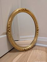 Full view of the vintage oval mirror showing the gold-toned ornate frame and clear mirror surface.