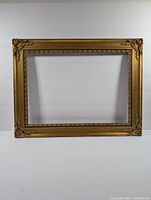 Front view of rectangular vintage wooden frame with ornate gold tone details and corner embellishments.