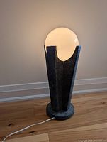 Side view of vintage pedestal lamp showing textured black base holding large white glass sphere lampshade, plugged in and illuminated.