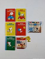 Photo showing six mini notebooks with colorful Snoopy-themed covers alongside mini coloured pencils pouch and Snoopy keychain