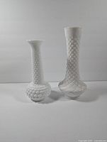 Front view of two white textured milk glass vases, one shorter with a bulbous bottom and hobnail pattern, one taller with diamond pattern.