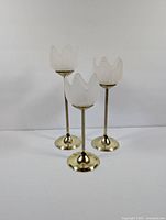 Front view of three vintage tulip-shaped tealight candle holders with brass bases and frosted glass.