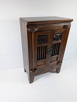 Front angled view of the wooden jewelry cabinet highlighting carved floral panels and door slats